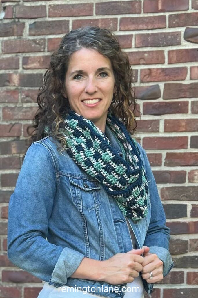 A woman wearing a denim jacket and tri-colored infinity scarf that is crocheted by hand.