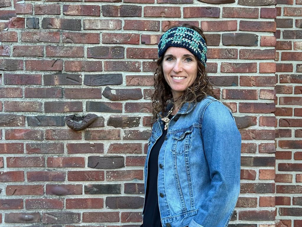 A friendly woman smiling and wearing a handmade crochet winter headband.