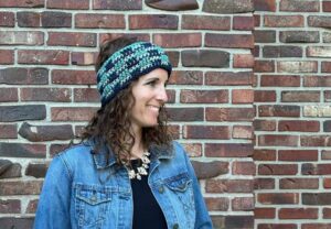 A friendly woman wearing a denim jacket and accessorizing with a crocheted ear warmer.