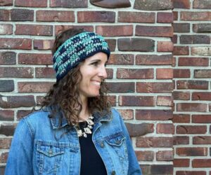 A friendly woman wearing a denim jacket and accessorizing with a crocheted ear warmer.