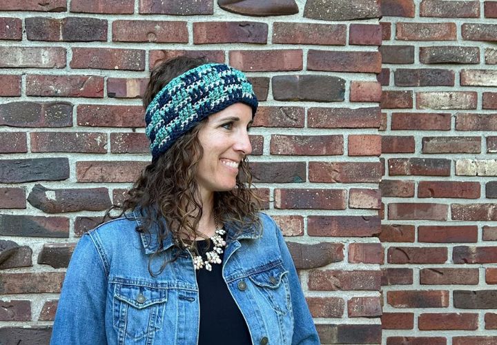 A friendly woman wearing a denim jacket and accessorizing with a crocheted ear warmer.