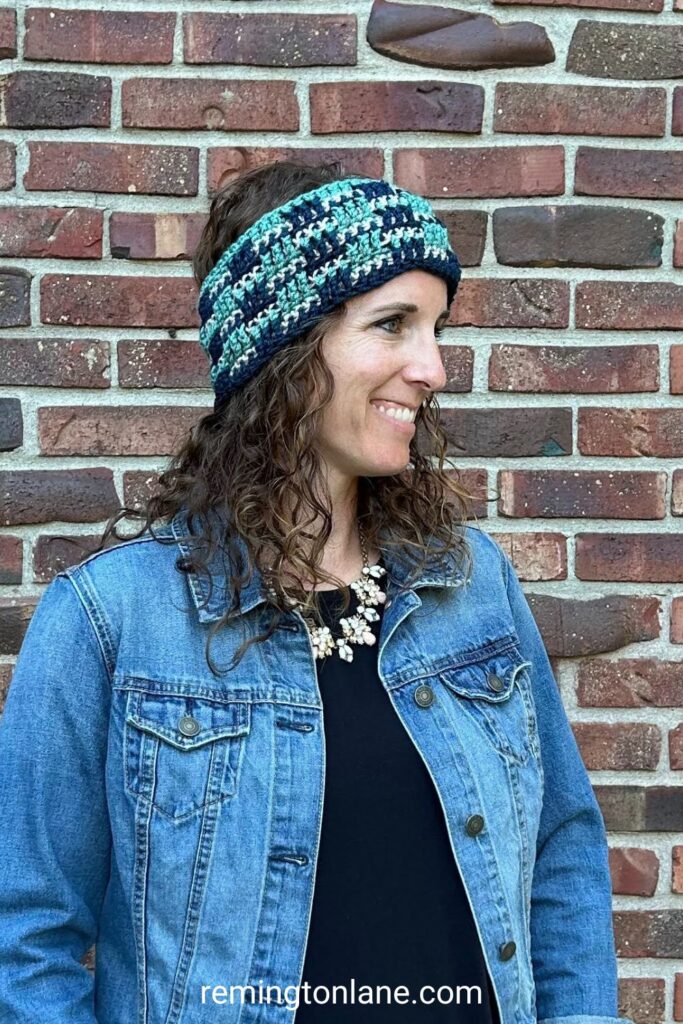 A close-up of a smiley woman bundled up for fall wearing a denim jacket and crochet ear warmer