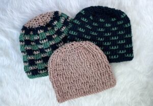 Three handmade winter hats in three pattern varieties - solid, two-color, and tri-color, laying on a white fur background.