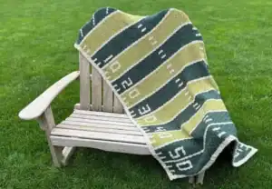 A crocheted blanket that looks like a football field, draped over a wooden bench.