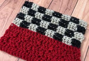 A close-up of a sample of a crochet blanket section that has a red stripe on the bottom and checkered flag look on top.