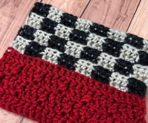 A close-up of a sample of a crochet blanket section that has a red stripe on the bottom and checkered flag look on top.