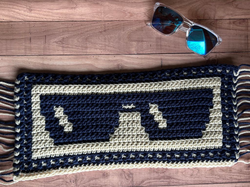 Mosaic crochet sunglasses blanket section lying next to real sunglasses on a table.